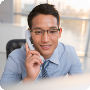 A businessperson speaks on a desk phone in an office. 